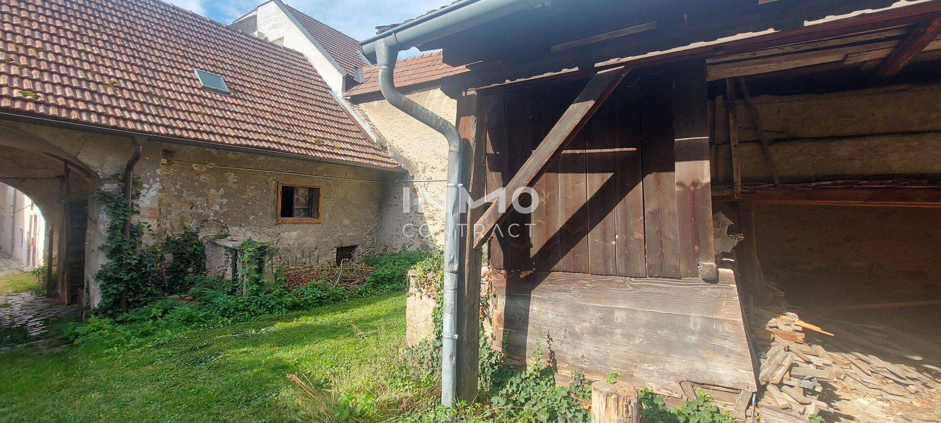 Historisches Gebäude mit Garten und alten Holzstrukturen im Außenbereich, umgeben von Natur.