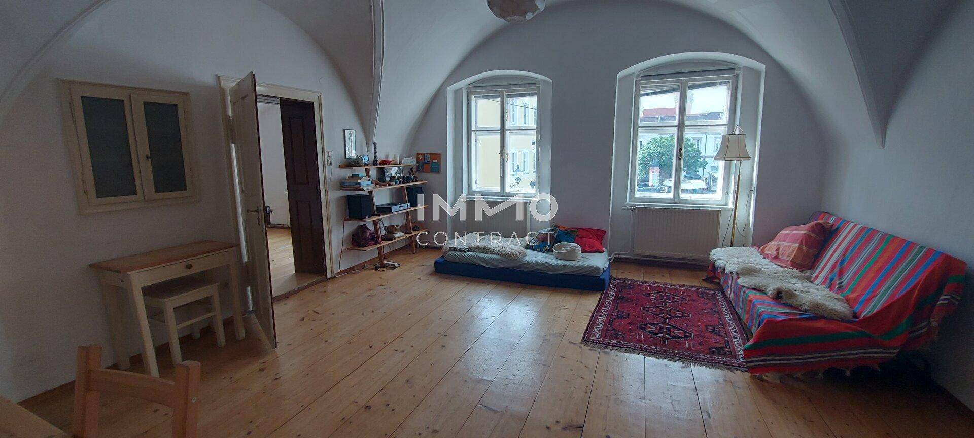 Helles Zimmer mit gewölbter Decke, Holzboden und Blick auf die Straße, gemütlich eingerichtet.