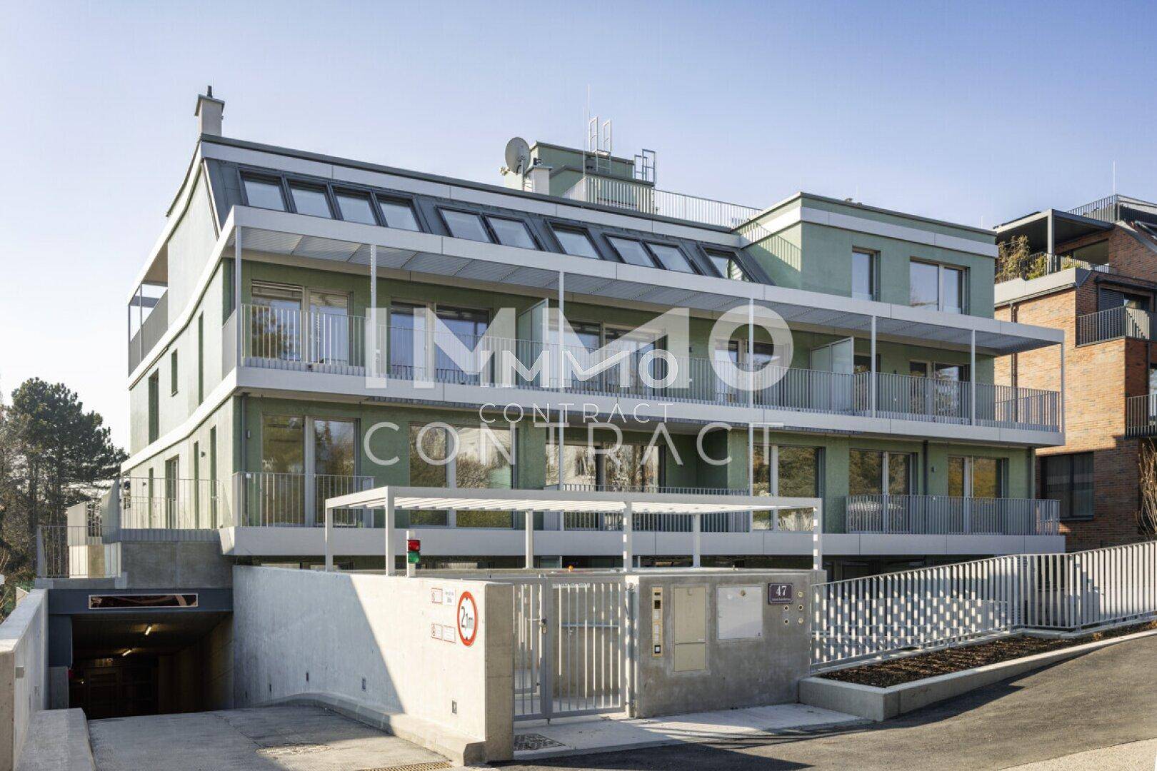 Außenansicht des modernen Apartmentgebäudes mit Zufahrt zur Tiefgarage und Balkonen.