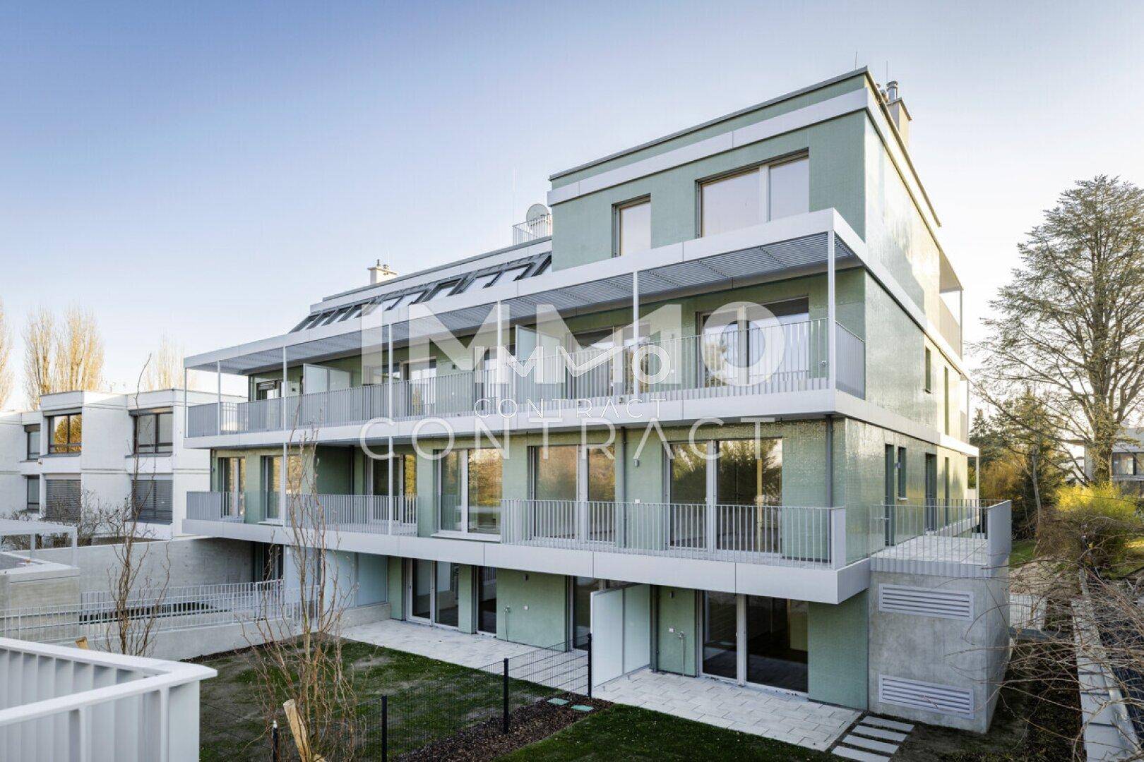 Seitenansicht des modernen Apartmentgebäudes mit mehreren Balkonen und umliegenden Grünflächen.