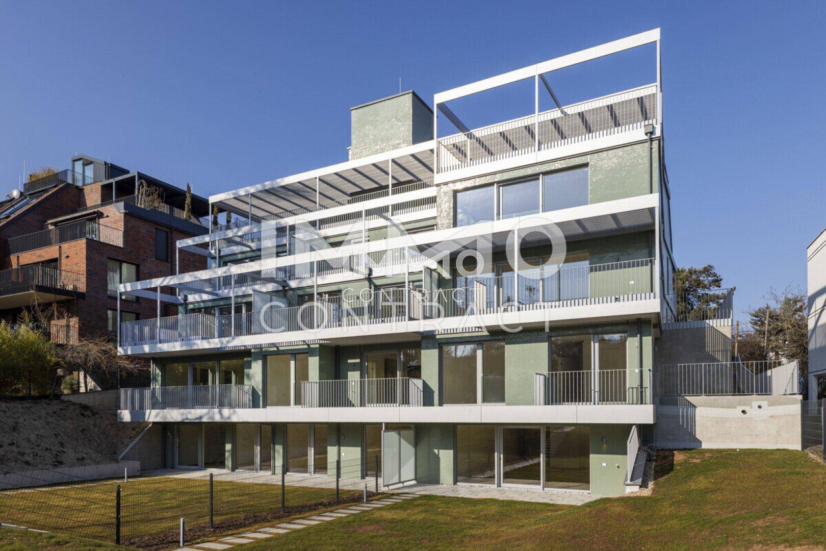 Rückansicht des modernen Apartmentgebäudes mit Rasenfläche und Balkonen unter blauem Himmel.