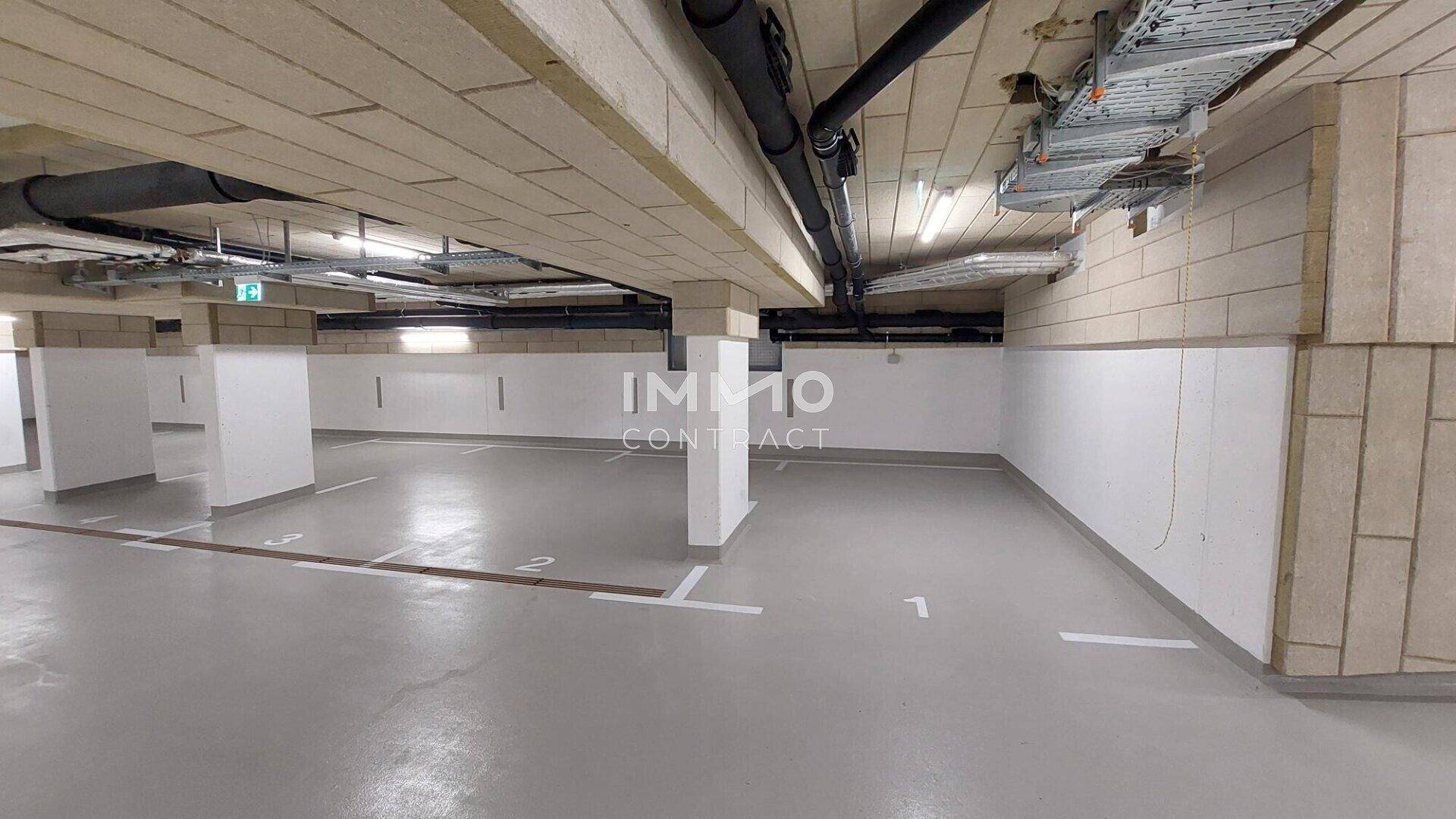Geräumige Tiefgarage mit markierten Stellplätzen und sichtbaren Installationen an der Decke.