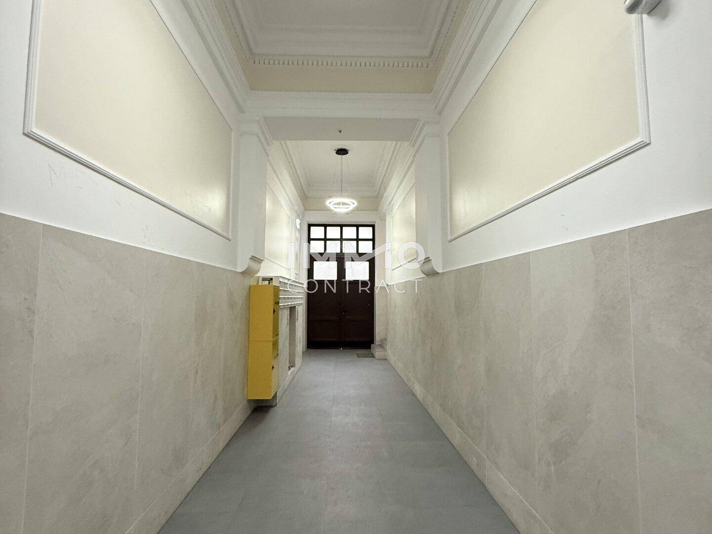 Langer Eingangsbereich mit hohen Decken, Stuckelementen und hellen Fliesen, führt zum Treppenhaus.