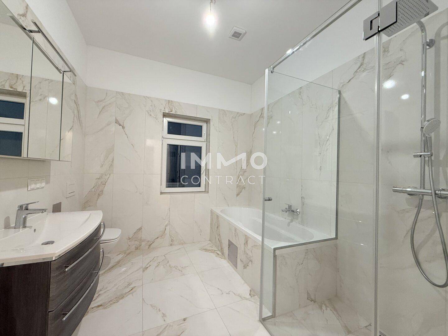 Modernes Badezimmer mit Marmorfliesen, Badewanne, begehbarer Dusche und großem Waschtisch.