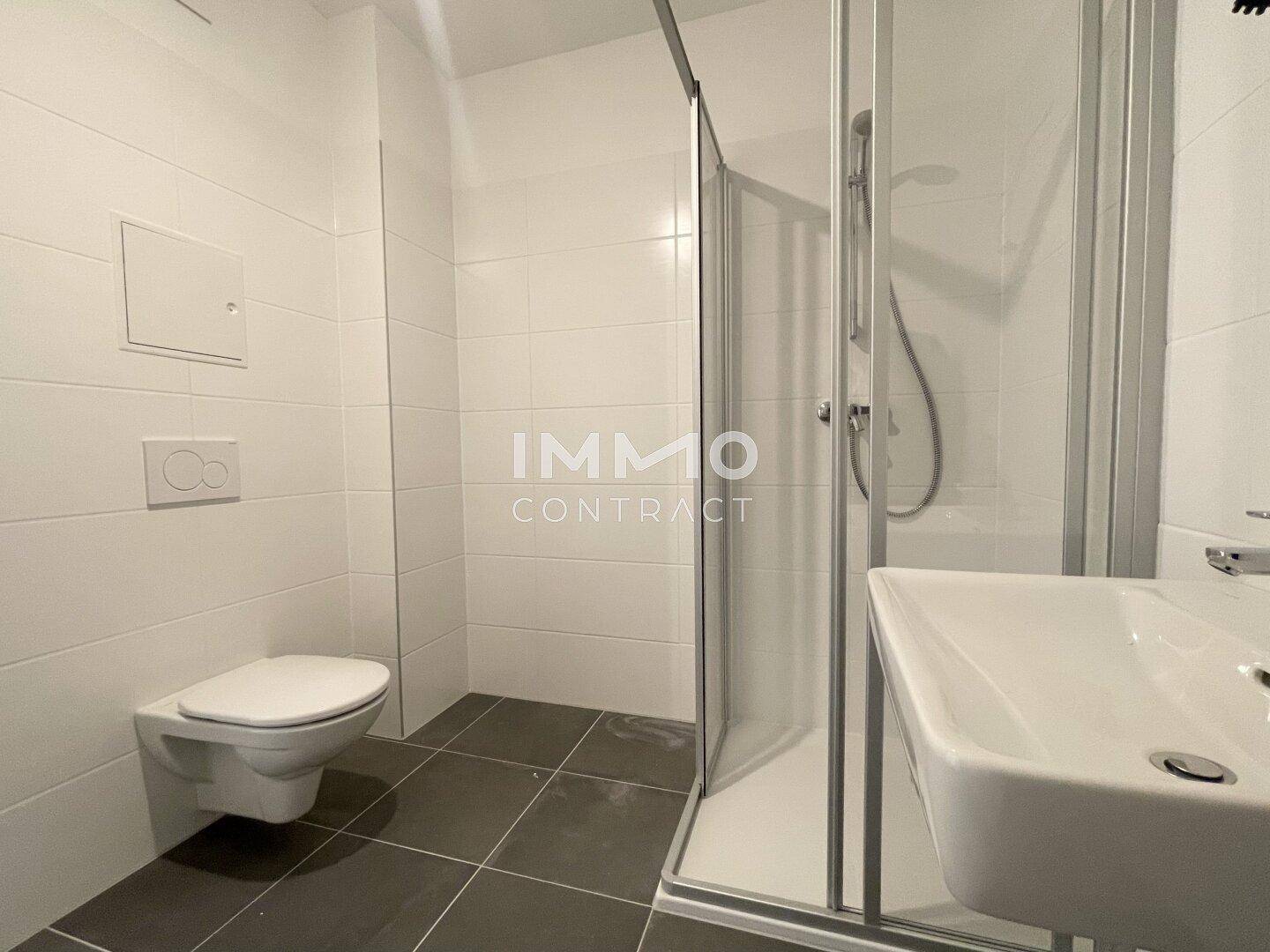 Modernes Badezimmer mit weißen Fliesen, Dusche und wandhängendem WC.