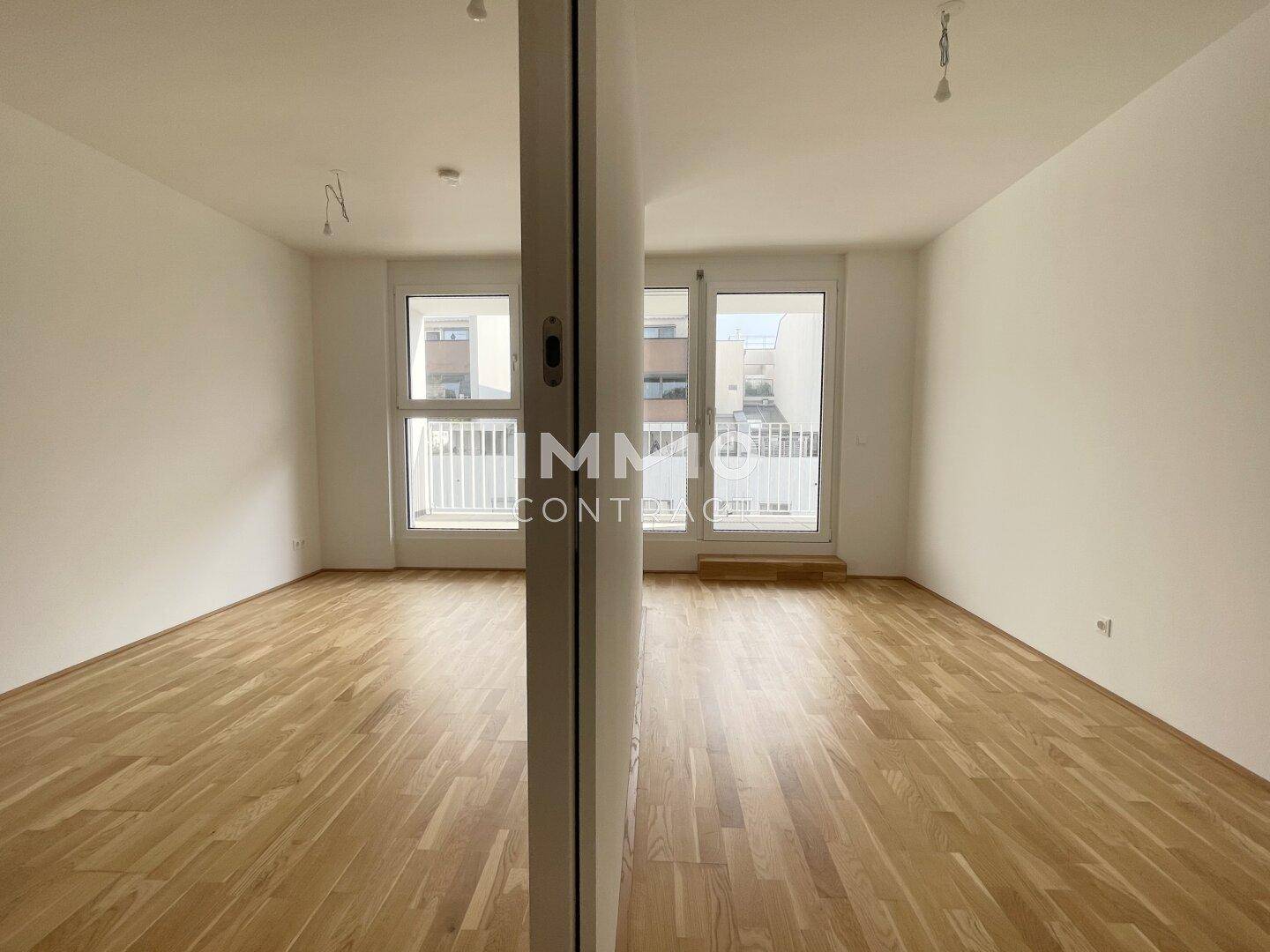 Heller Wohnbereich mit Parkettboden und Zugang zu einem Balkon, ideal für offenes Wohnen.