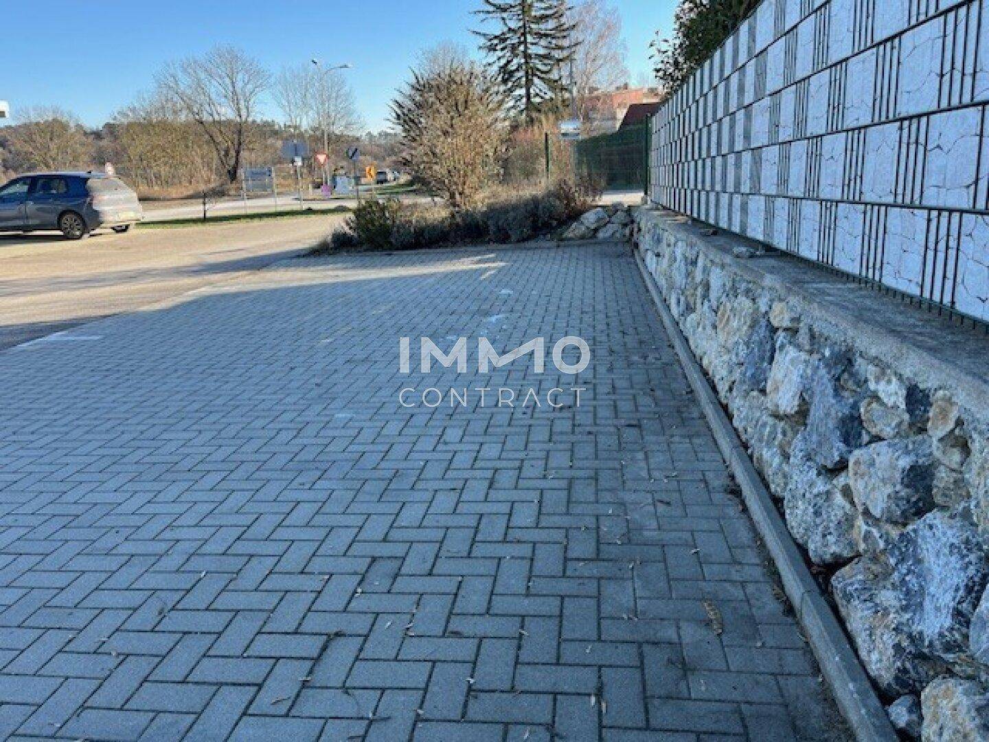 Außenparkplatz mit grauen Pflastersteinen und einer dekorativen Steinmauer entlang der Grundstücksgrenze.