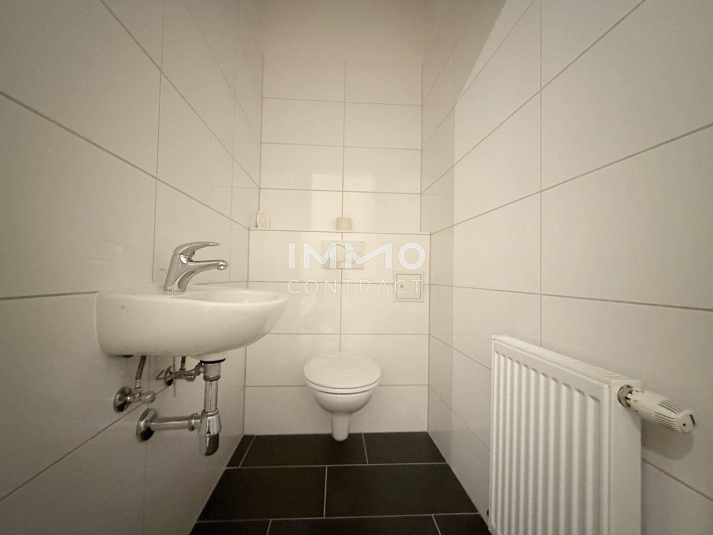 Kleines Gäste-WC mit modernem Waschbecken, wandhängender Toilette und dunklen Bodenfliesen.