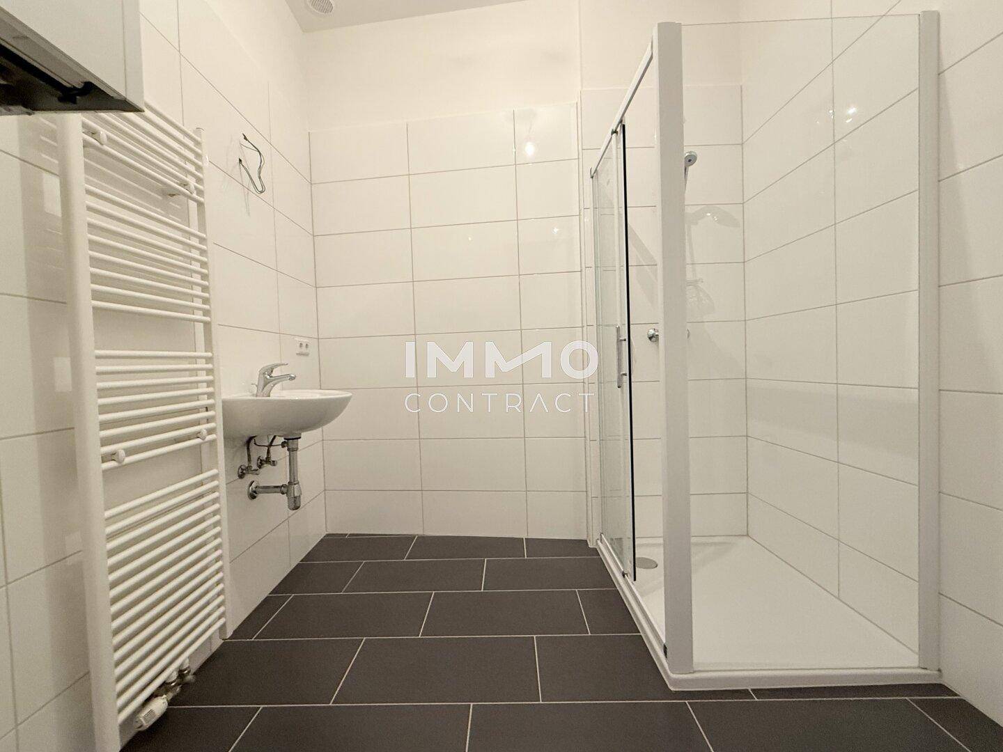 Modernes Badezimmer mit weiß gefliesten Wänden, dunklem Boden und einer geräumigen Duschkabine.