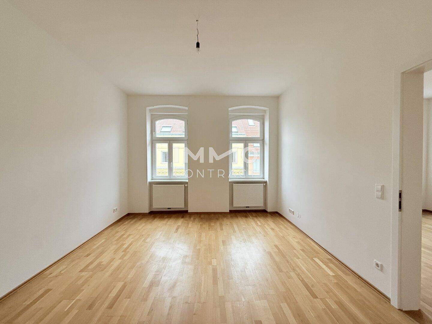 Geräumiges, helles Zimmer mit Holzboden und hohen Decken, ideal für Wohn- oder Schlafbereich.