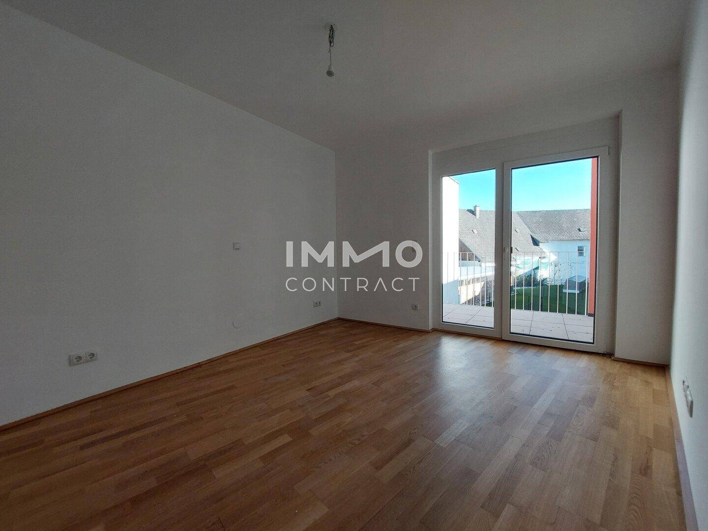 Helles Zimmer mit Parkettboden und Zugang zu einem Balkon, ideal als Schlafzimmer.