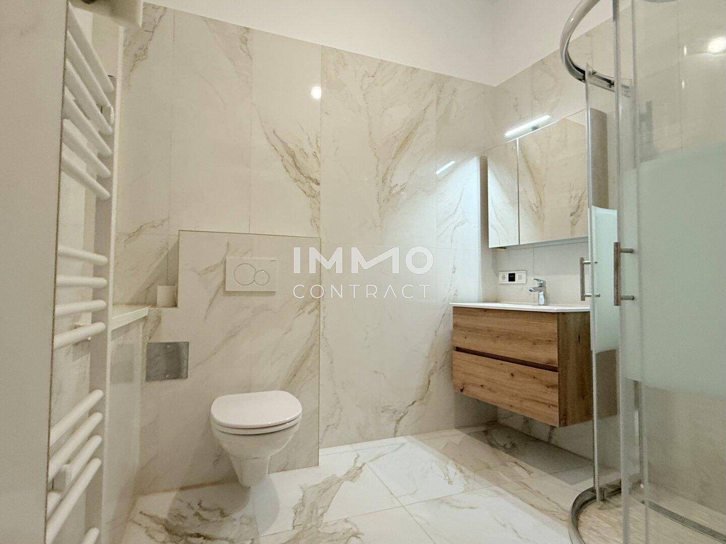 Modernes Badezimmer mit Marmorfliesen, Dusche, WC und Holzwaschtischunterschrank.