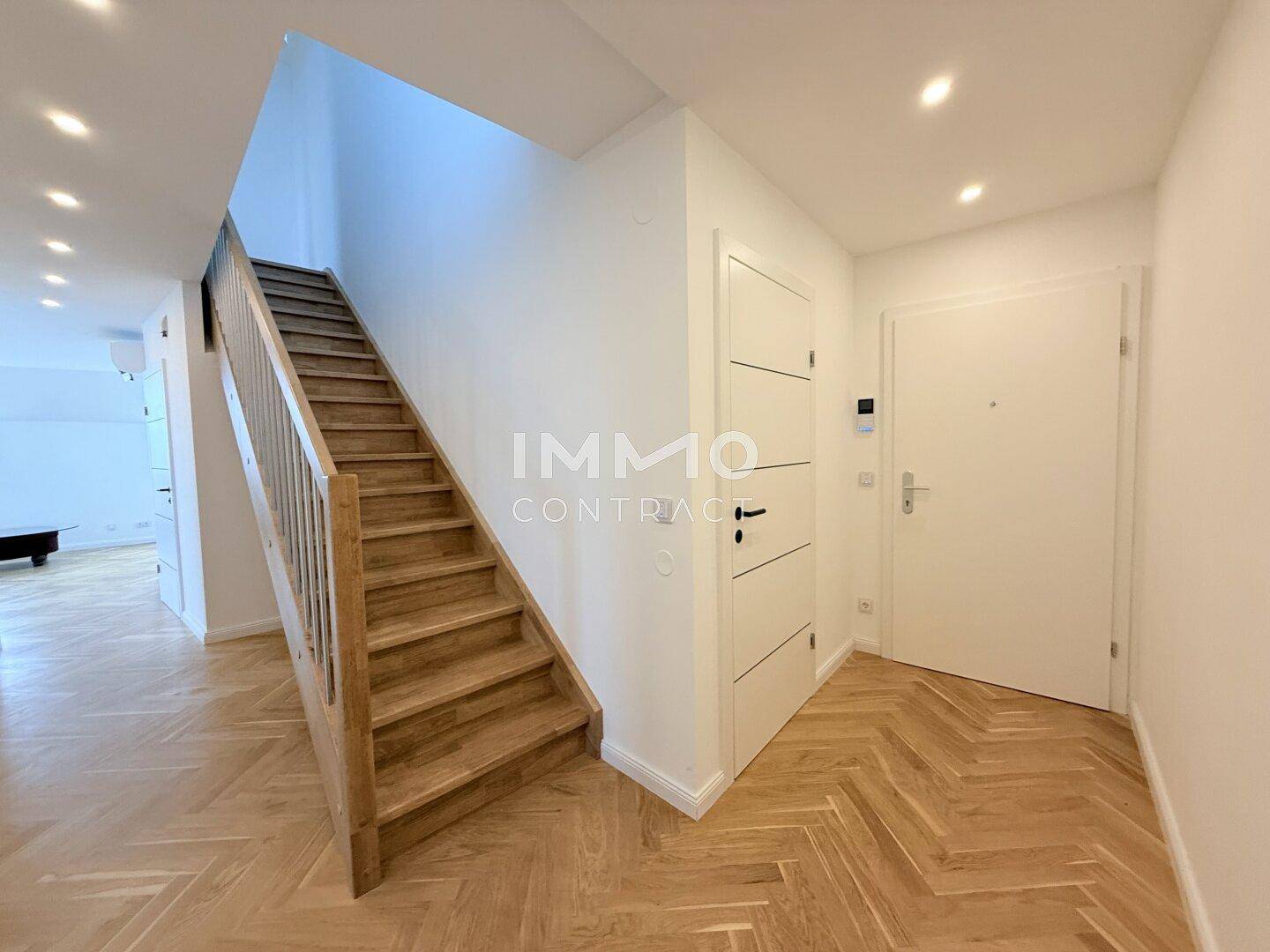 Heller Eingangsbereich mit Holztreppe und modernem Fischgrätparkettboden.