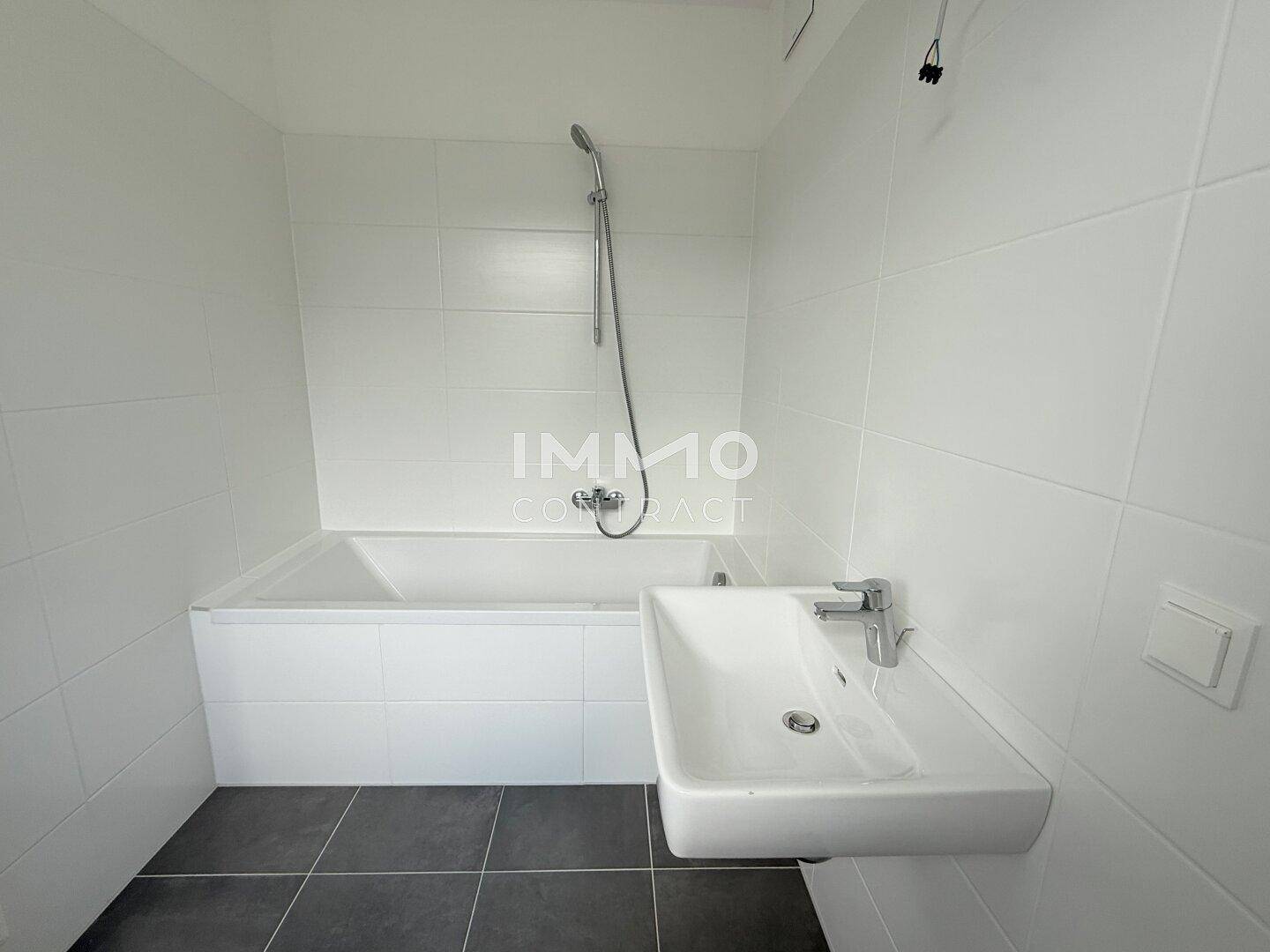 Modernes Badezimmer mit weißer Badewanne, Waschbecken und grauen Bodenfliesen.