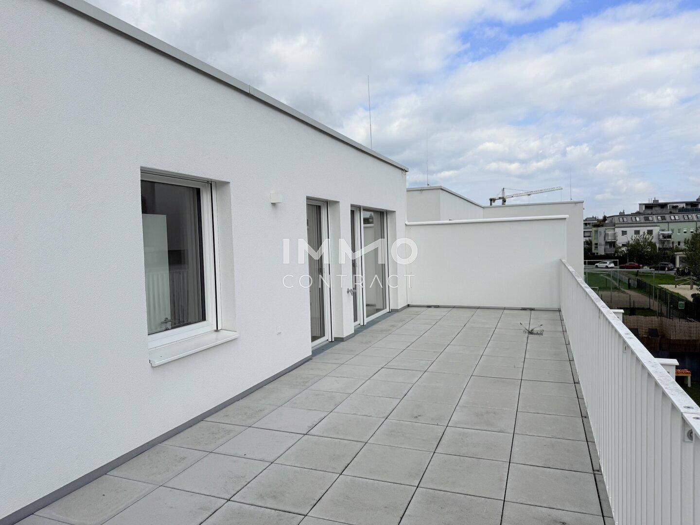 Weitläufige Dachterrasse mit hellen Fliesen und moderner Architektur, bietet viel Platz im Freien.