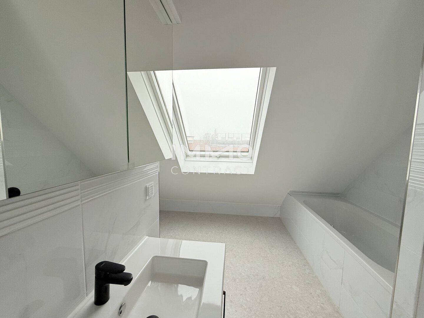 Helles Badezimmer im Dachgeschoss mit Badewanne, Waschtisch und großem Dachfenster.