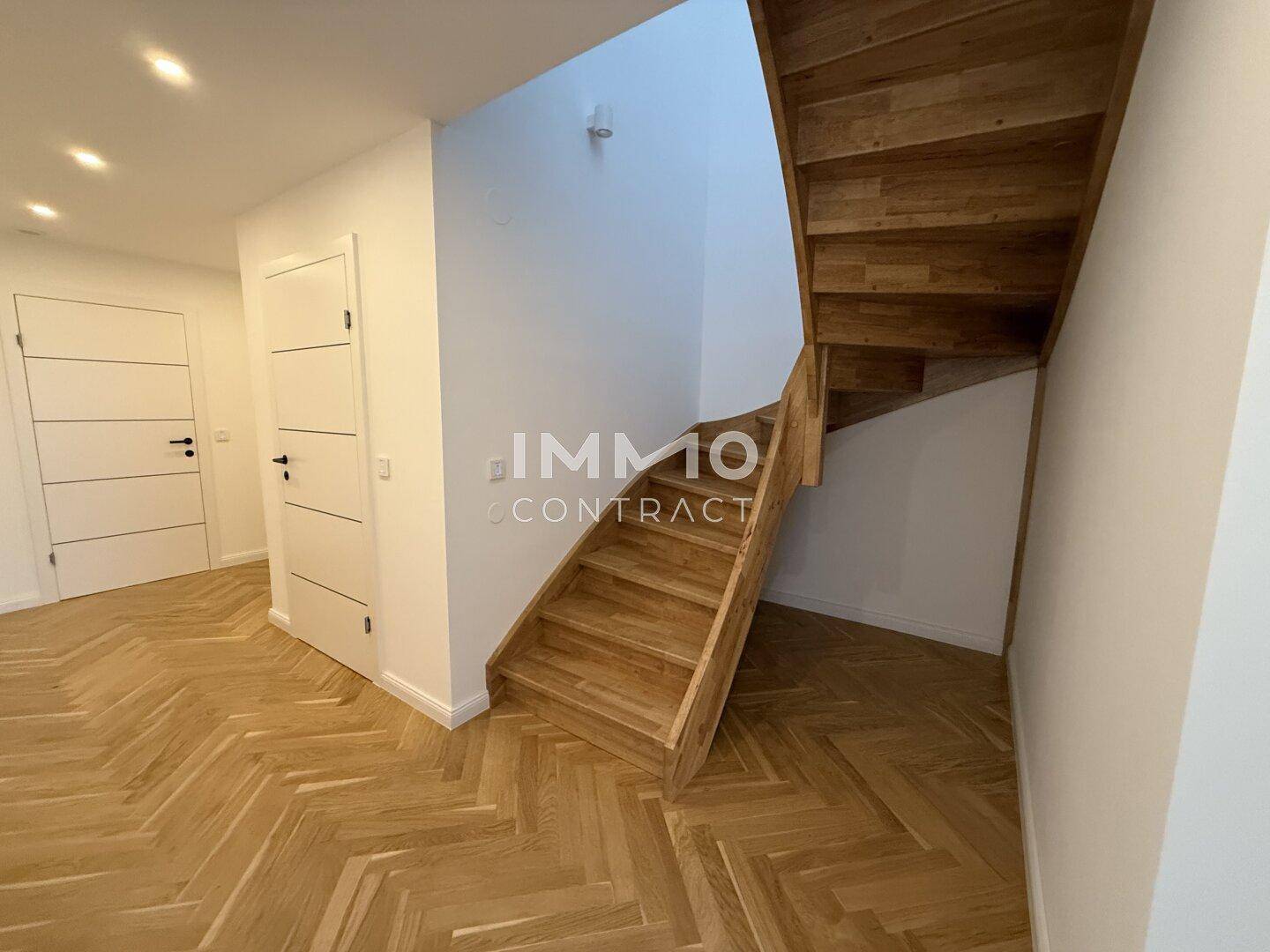 Heller Flur mit Fischgrätparkett und einer eleganten Holztreppe, die in die obere Etage führt.