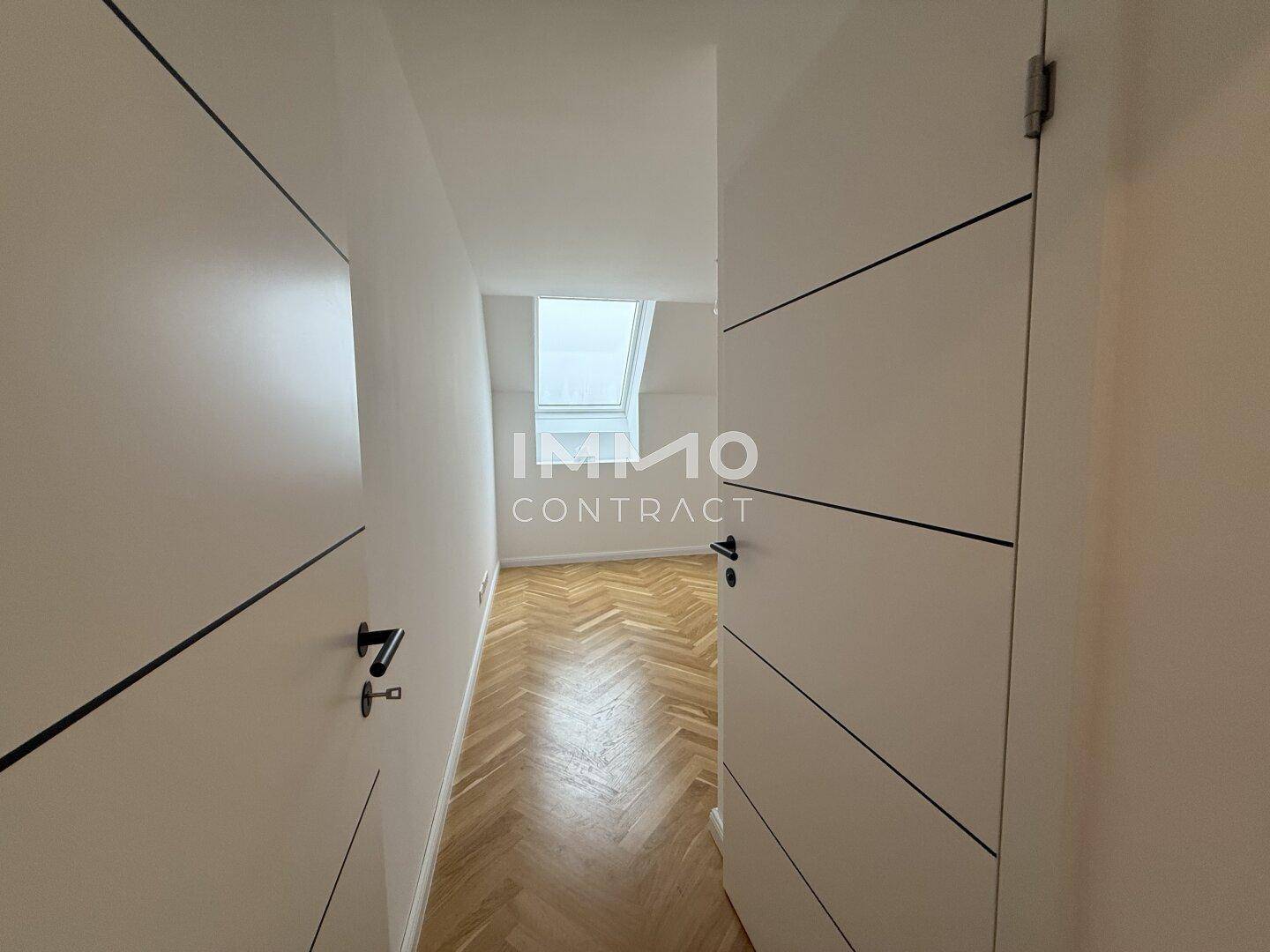 Schmaler Flur mit Fischgrätparkett und einem Dachfenster am Ende, das Helligkeit spendet.