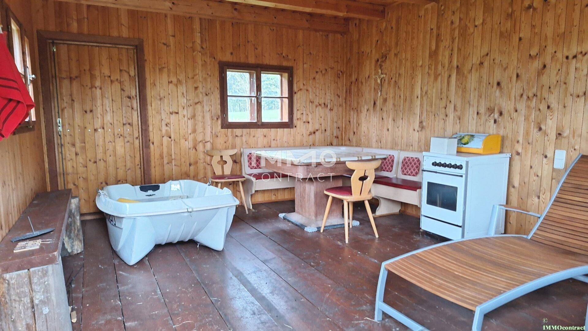 Rustikaler Innenraum einer Holzhütte mit Holzboden, Sitzgelegenheiten, Kochstelle und Whirlpool.
