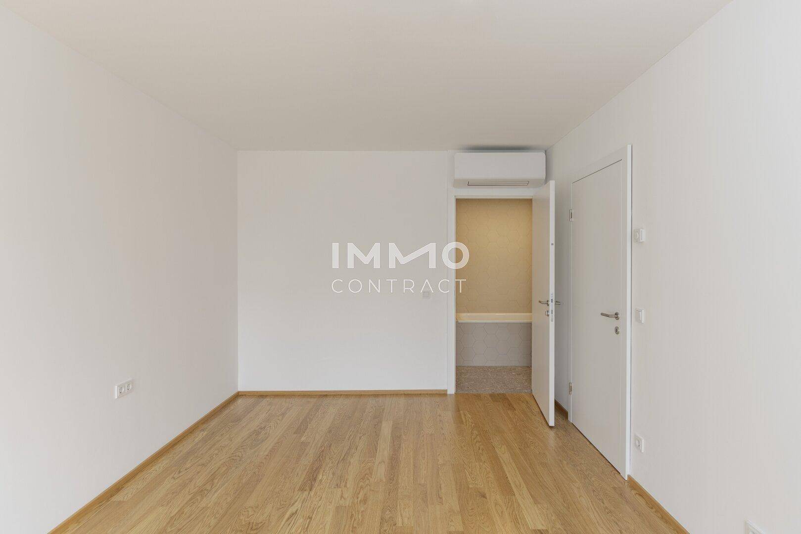 Helles Zimmer mit Holzboden, Klimaanlage und einem praktischen begehbaren Schrankbereich.