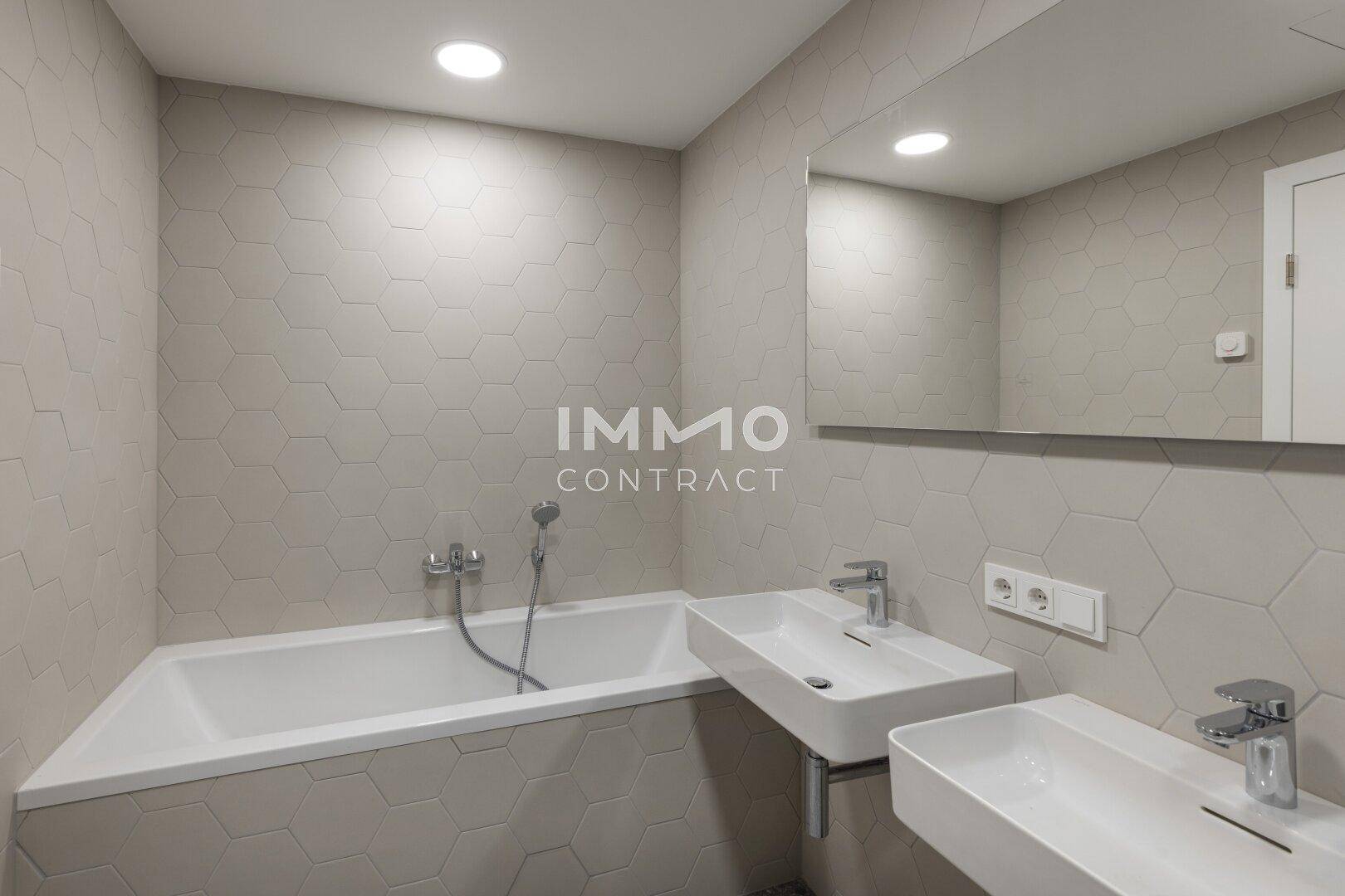 Helles Badezimmer mit Badewanne, Doppelwaschbecken und modernen sechseckigen Fliesen.