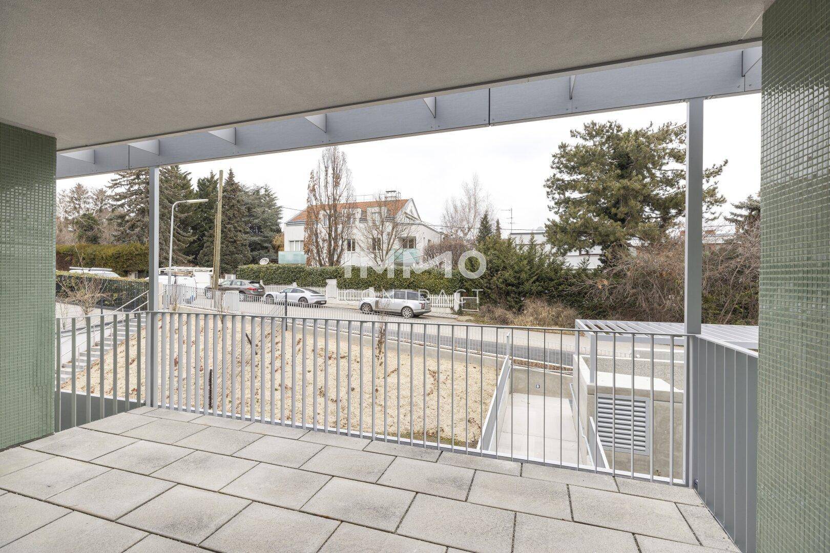Geräumiger Balkon mit Fliesenboden und Blick auf die Straße und Bäume.