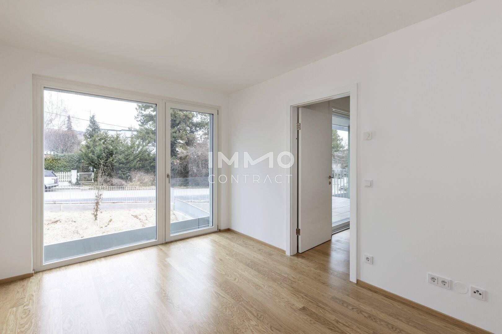 Heller Raum mit Holzboden und großen Fenstern zur Straße hin.
