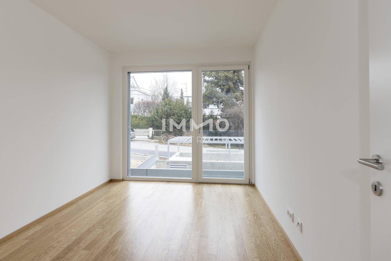 Helles Zimmer mit Holzboden und großem Fenster, das viel Tageslicht hereinlässt.