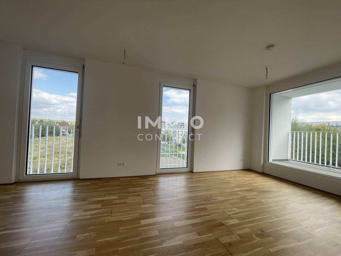 Geräumiger Wohnraum mit hellem Parkettboden und Zugang zu einem Balkon mit Weitblick.