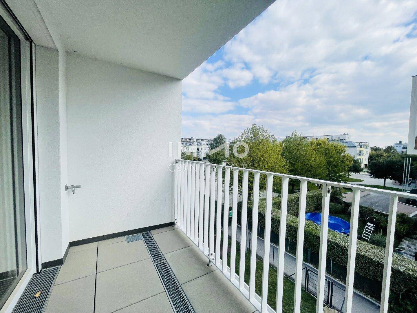 Moderner Balkon mit weißem Geländer und Blick auf die umliegende Grünfläche und Gebäude.