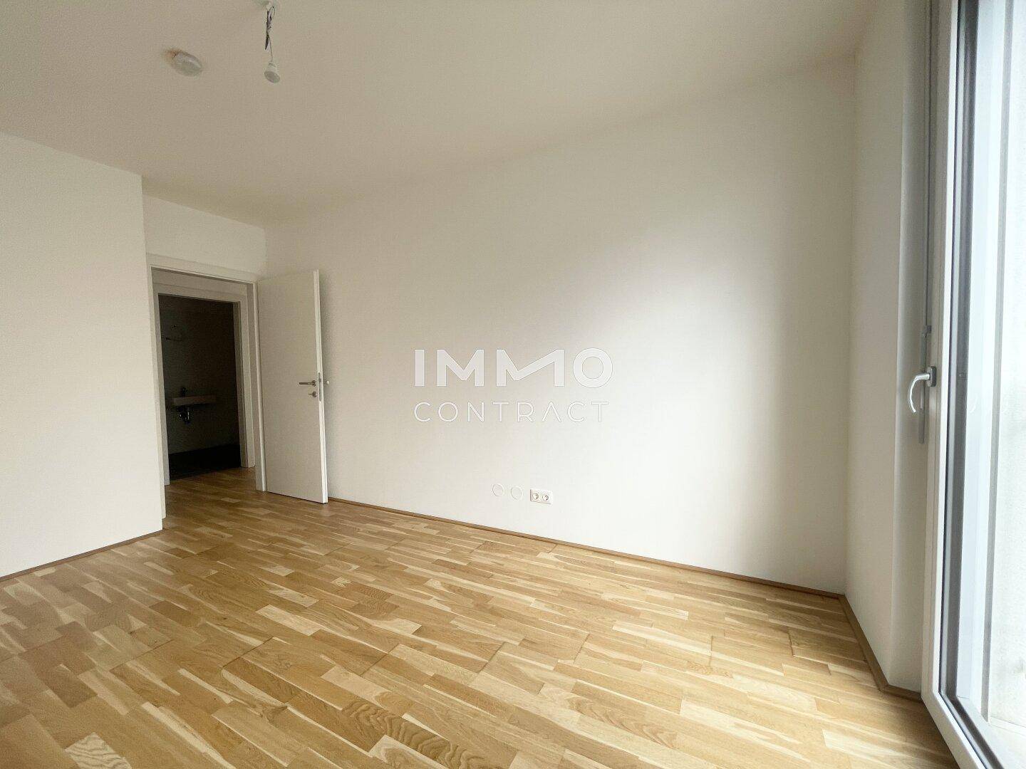 Helles Zimmer mit Parkettboden und offener Tür zu einem angrenzenden Badezimmer oder WC.