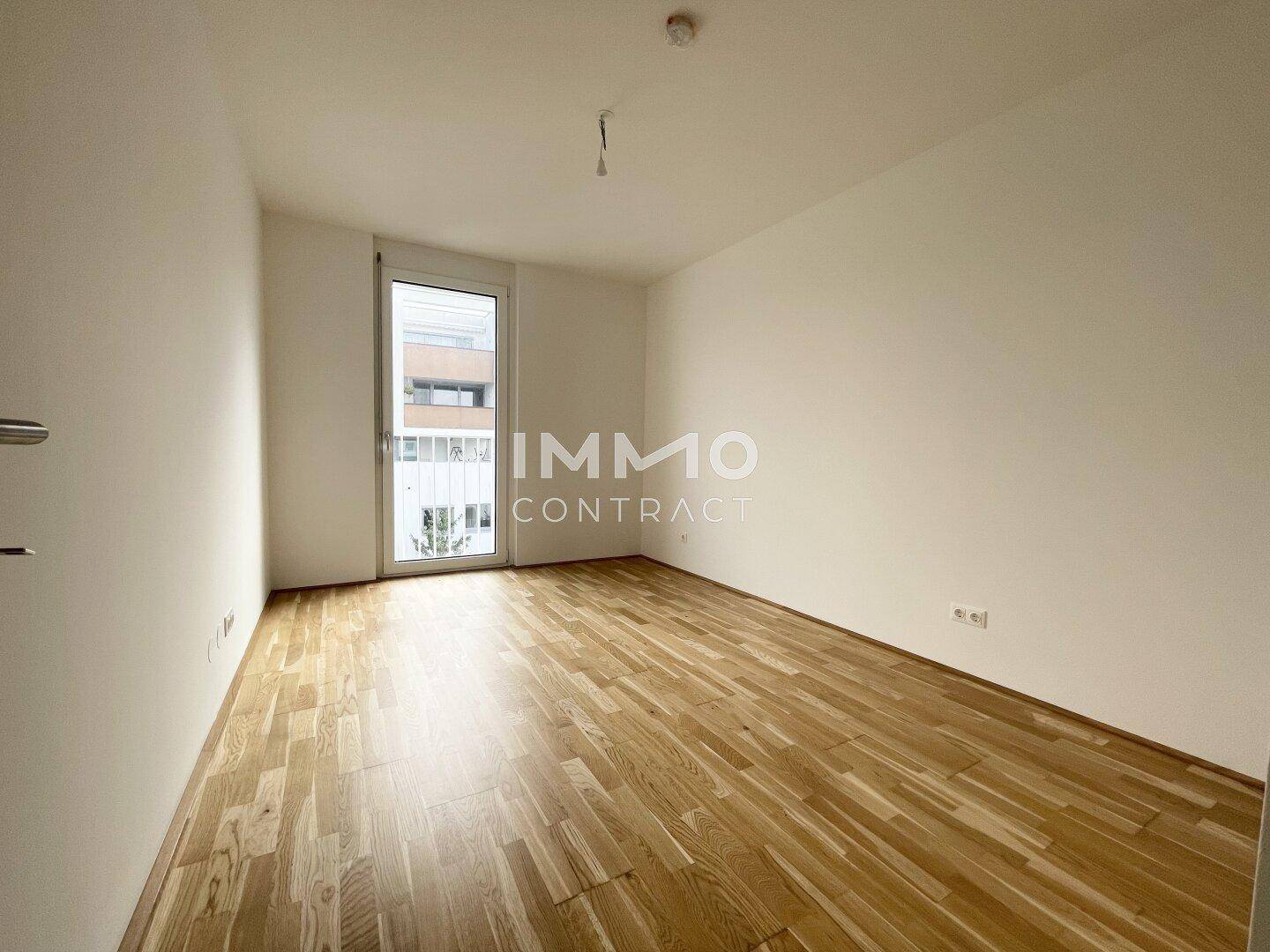 Leeres Schlafzimmer mit Parkettboden und einer Balkontür, die Zugang zum Außenbereich bietet.