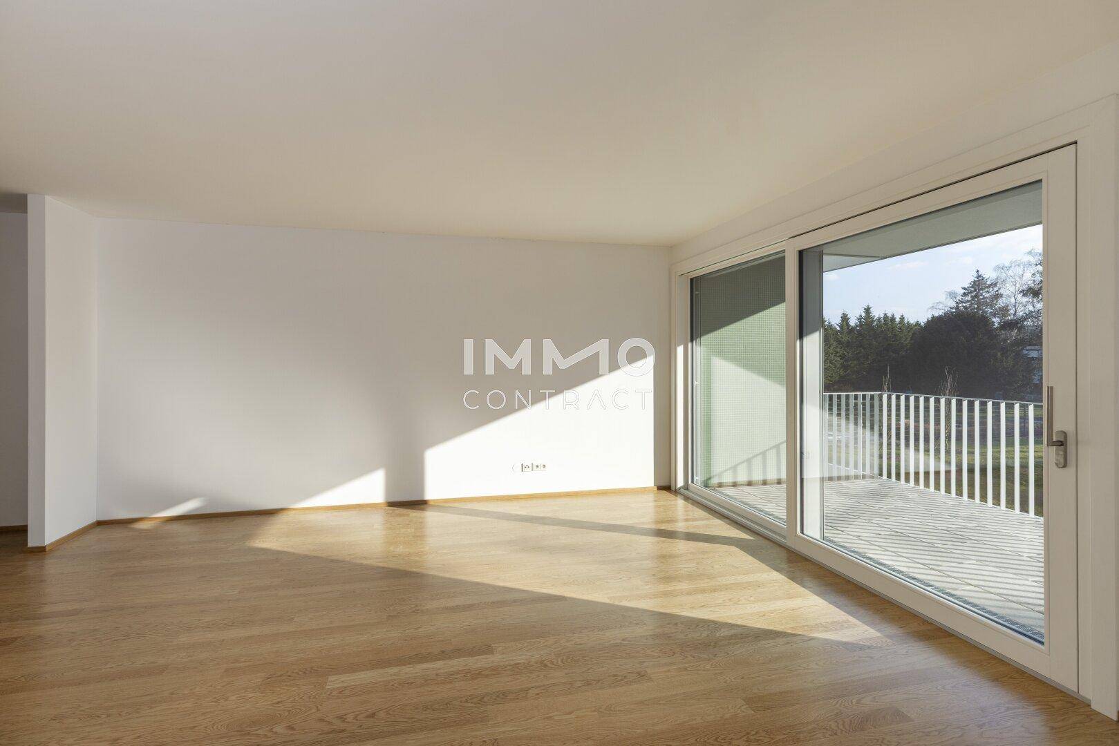 Geräumiges Wohnzimmer mit Holzboden und breiter Schiebetür zum Balkon, sehr hell und offen.