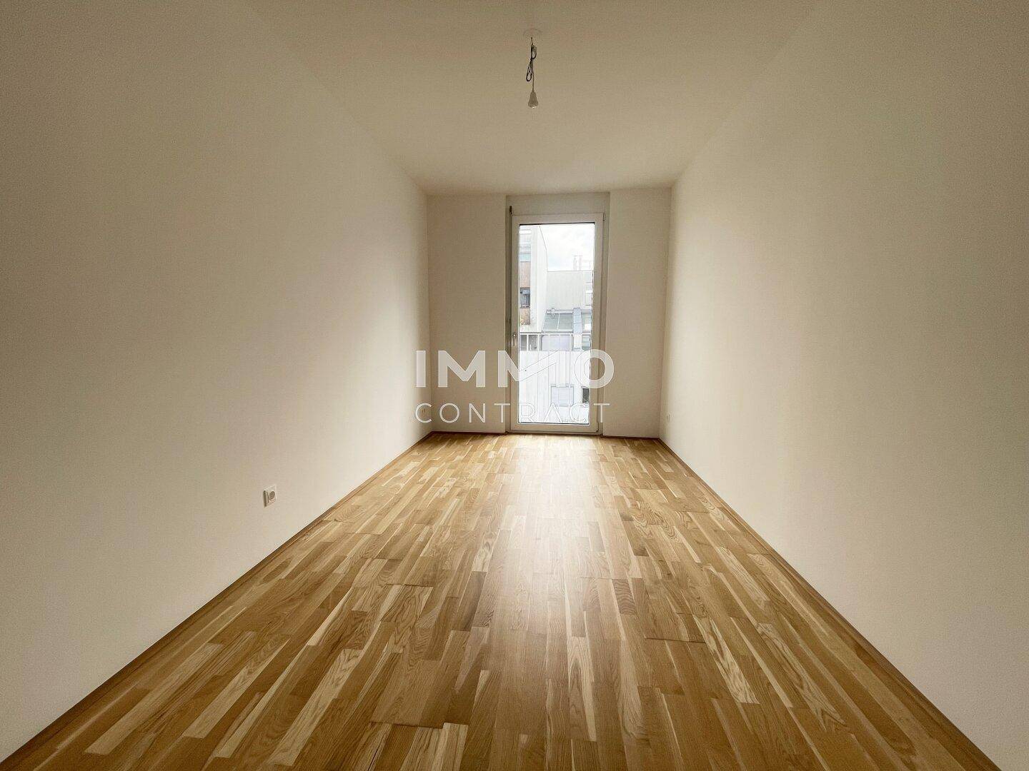 Geräumiges Zimmer mit Parkettboden und einer großen Balkontür, die für viel Helligkeit sorgt.
