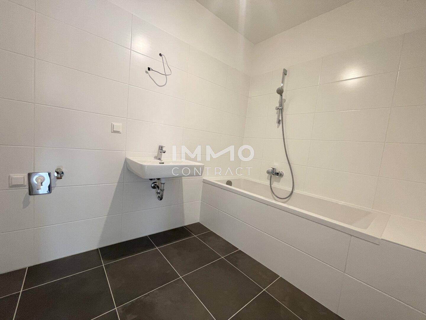 Modernes Badezimmer mit weißen Wandfliesen, dunklem Boden und einer Badewanne mit Duschfunktion.