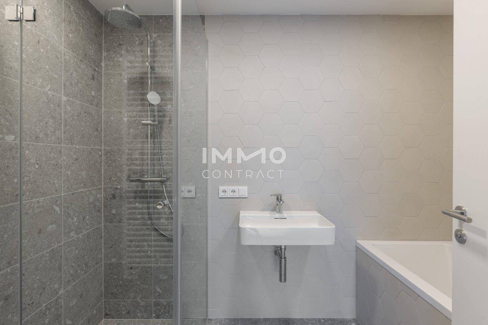 Modernes Badezimmer mit grauen Fliesen, Dusche und Badewanne.