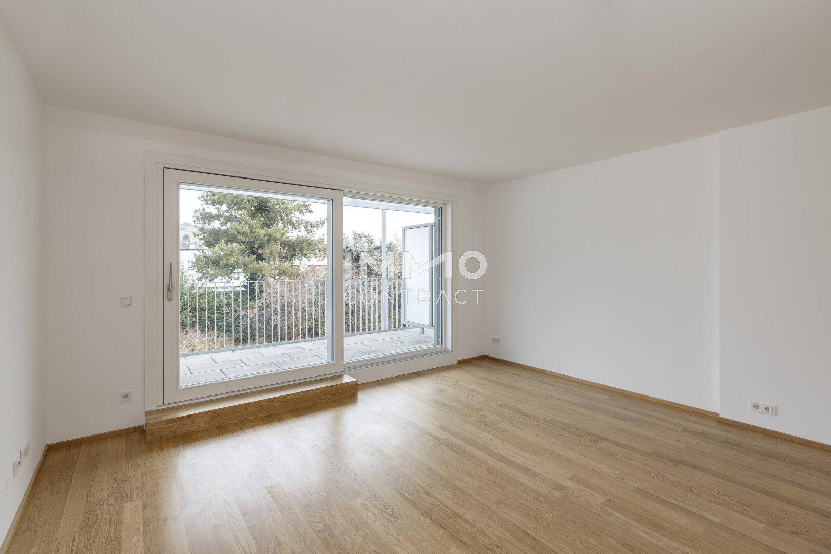 Helles, leeres Zimmer mit Eichenparkettboden und großem Schiebefenster zum Balkon.