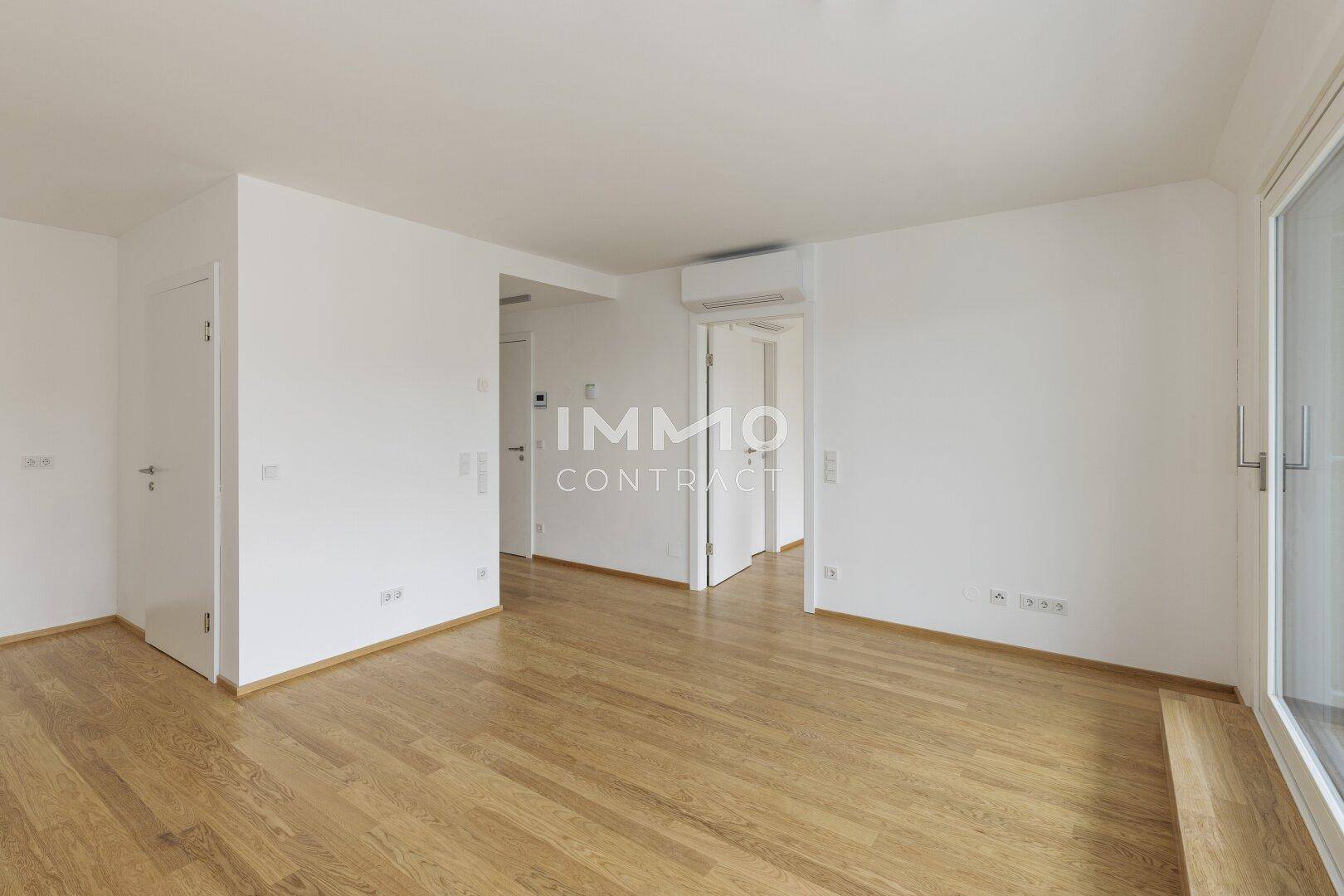 Geräumiges, leeres Zimmer mit Holzboden, weißen Wänden und Zugang zu weiteren Räumen.