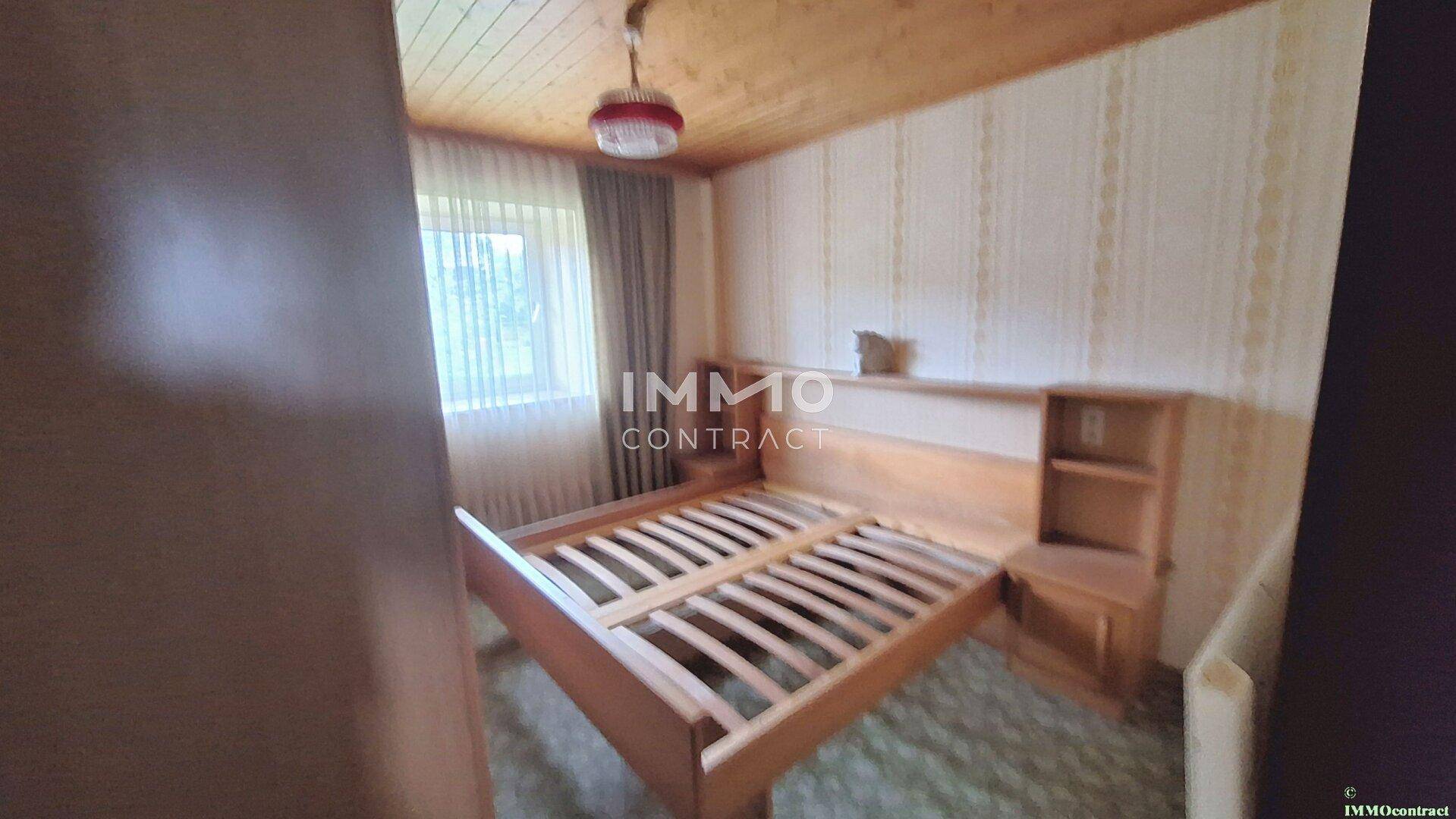 Schlafzimmer mit Holzdecke, Teppichboden und einfachem Holzbett, renovierungsbedürftig.