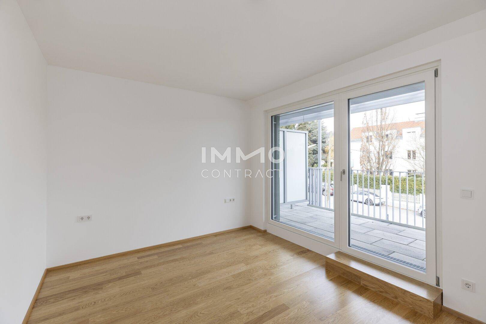 Lichtdurchflutetes Zimmer mit Parkettboden und breiter Schiebetür, die auf einen Balkon führt.
