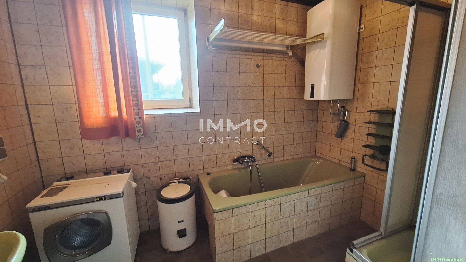 Badezimmer mit grüner Badewanne, Fliesen und Waschmaschine, in die Jahre gekommen.