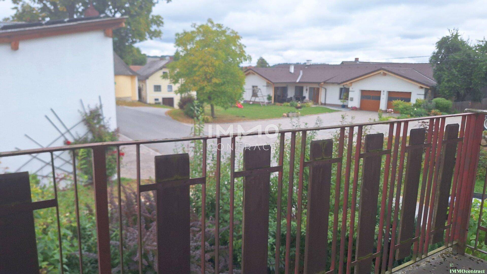 Blick vom Balkon auf die ländliche Umgebung mit weiteren Häusern und viel Grün.