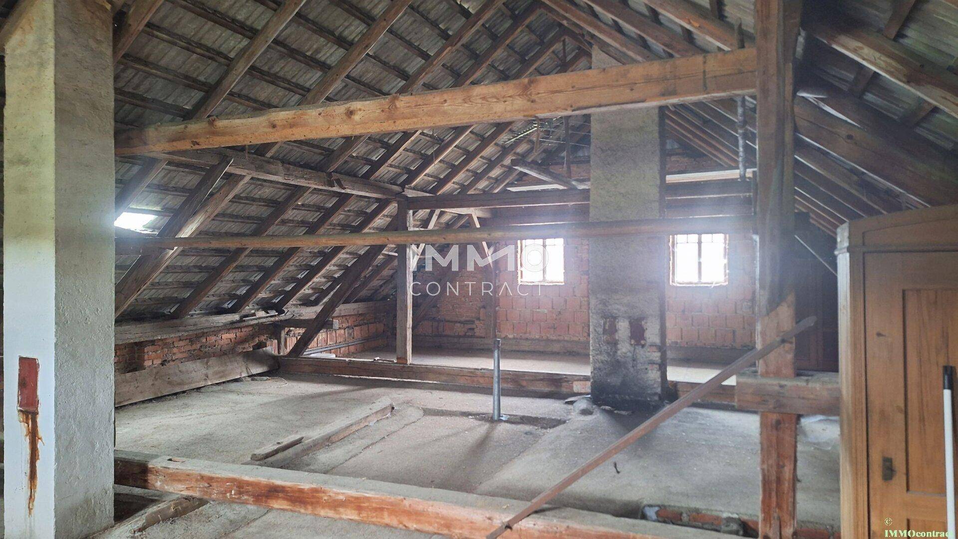 Geräumiger Dachboden mit sichtbaren Holzbalken und Fenstern, ideal für Ausbauprojekte.