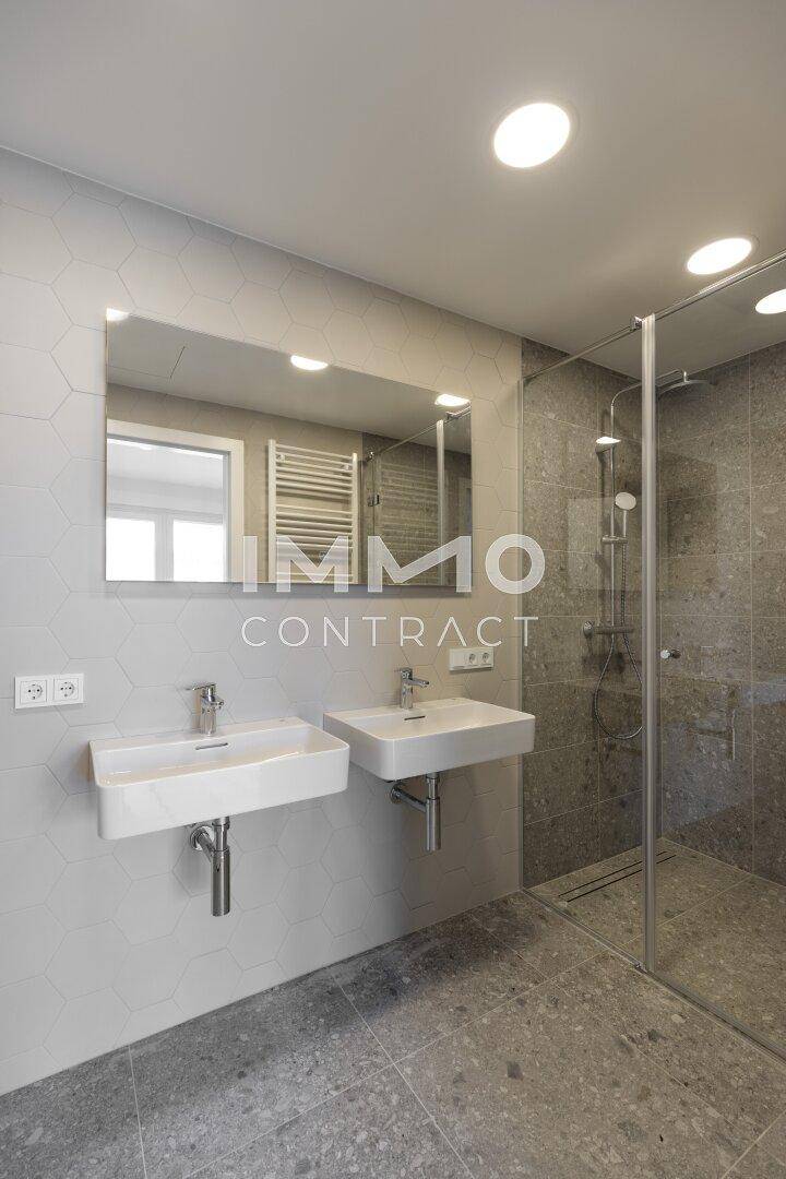 Modernes Badezimmer mit Doppelwaschbecken, grauen Fliesen und einer begehbaren Dusche.