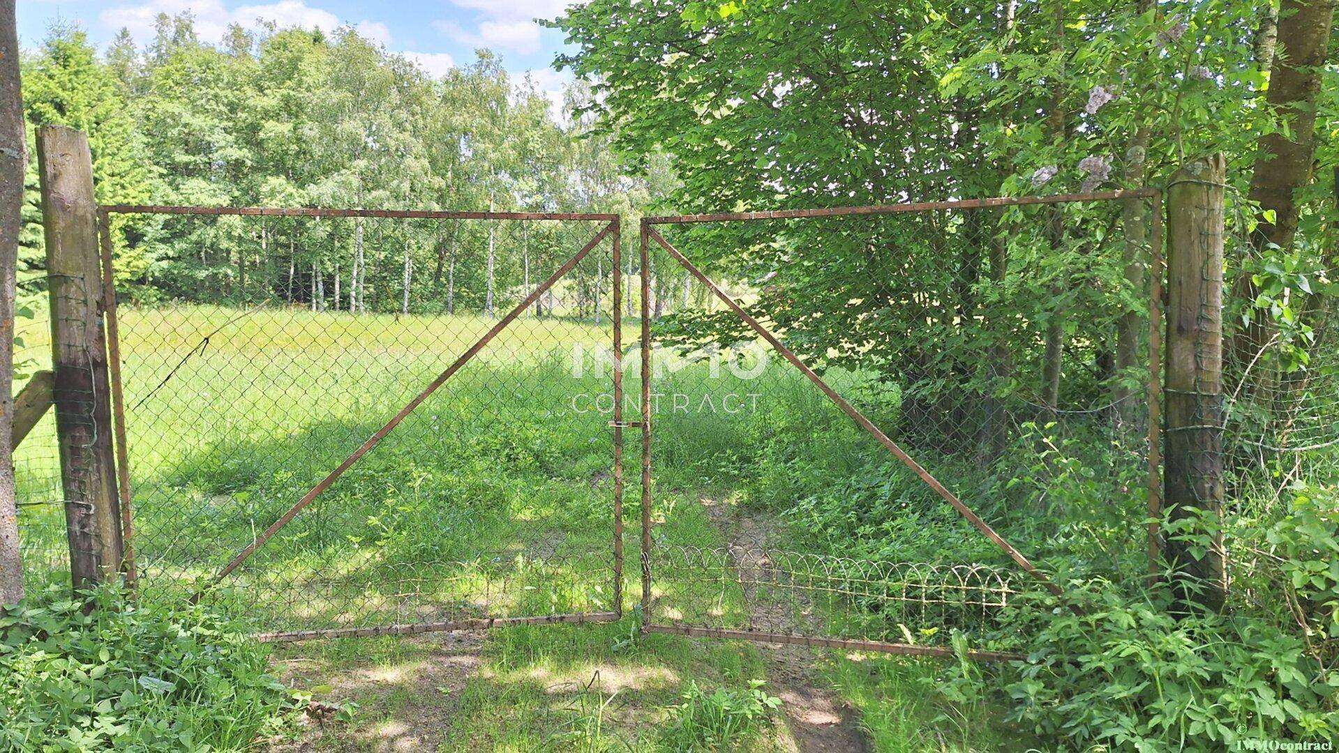 Rostiges Metalltor, das zu einer weiten grünen Wiese führt, umgeben von Bäumen.