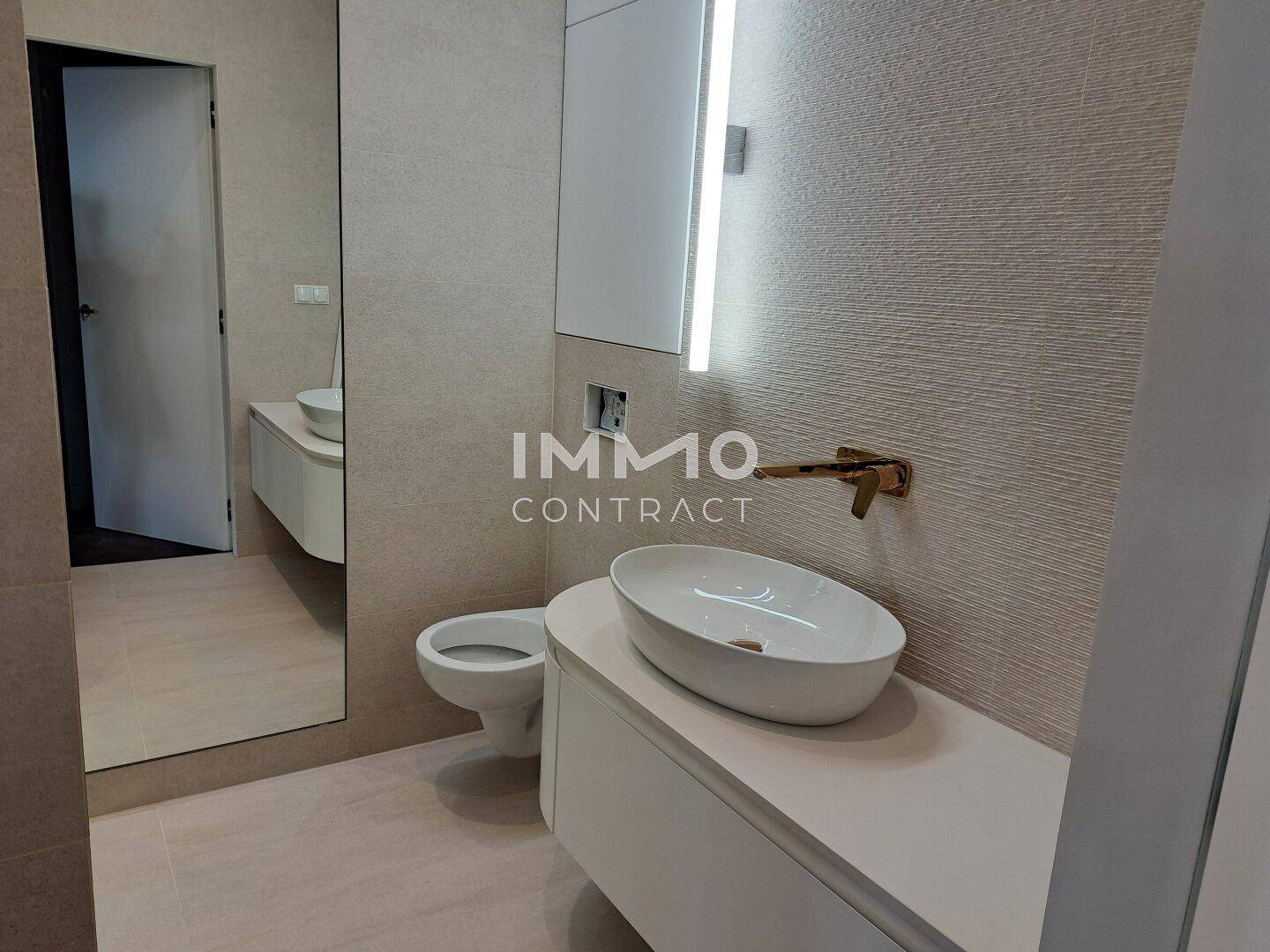 Modernes Badezimmer mit elegantem Aufsatzwaschbecken, großem Spiegel und goldfarbenen Armaturen.