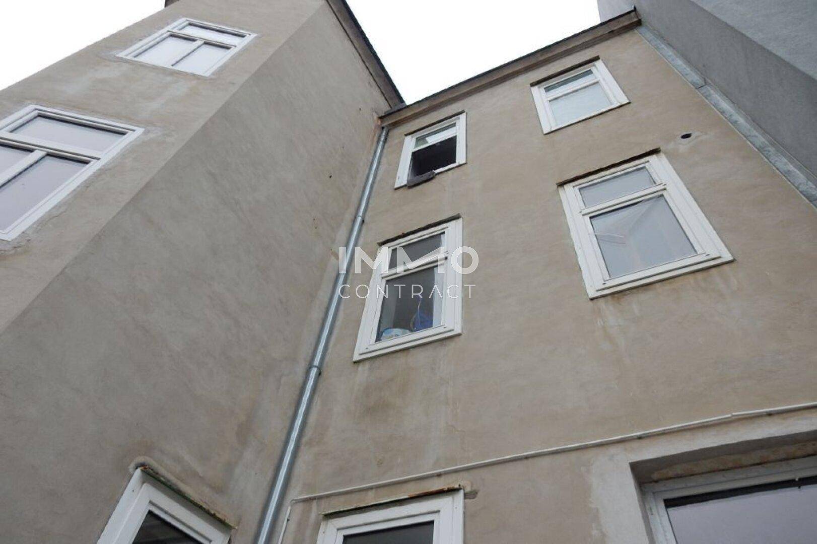Rückseite eines Wohngebäudes mit mehreren Fenstern und einfacher Putzfassade.