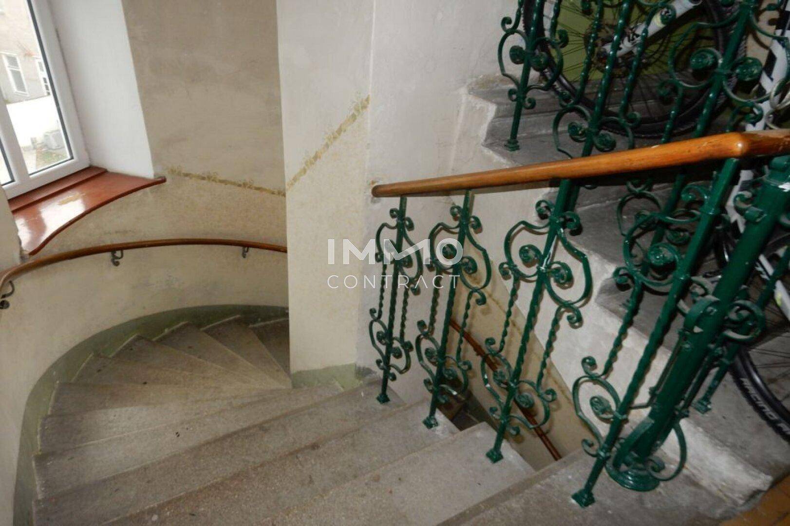 Historisches Treppenhaus mit schmiedeeisernem Geländer und Steinstufen in einem Altbau.