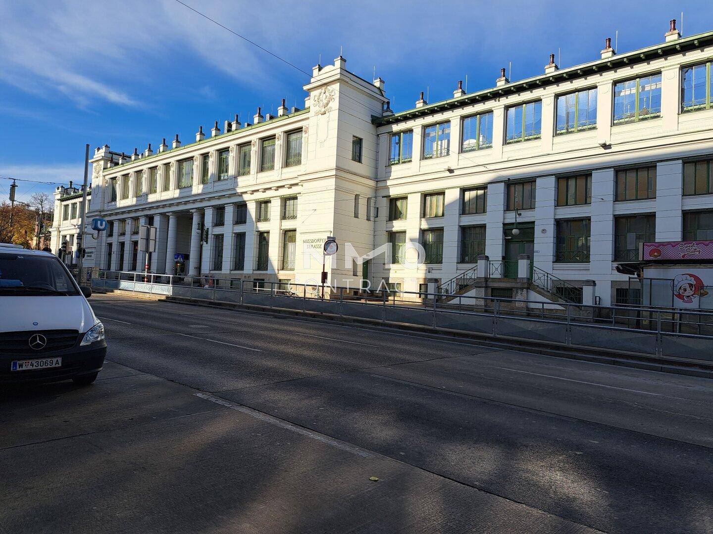 Historisches Gebäude mit klassischer Architektur und großen Fenstern an einer belebten Straße.