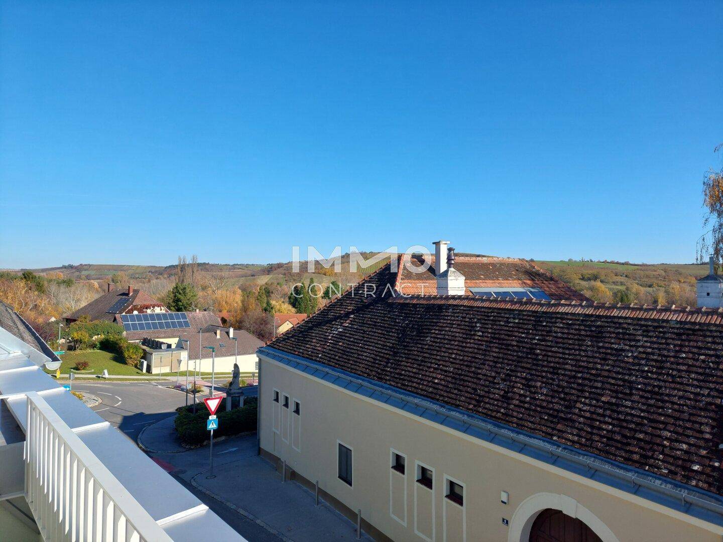 Weitblick über eine ländliche Umgebung mit Häusern, Straßen und grünen Hügeln unter blauem Himmel.